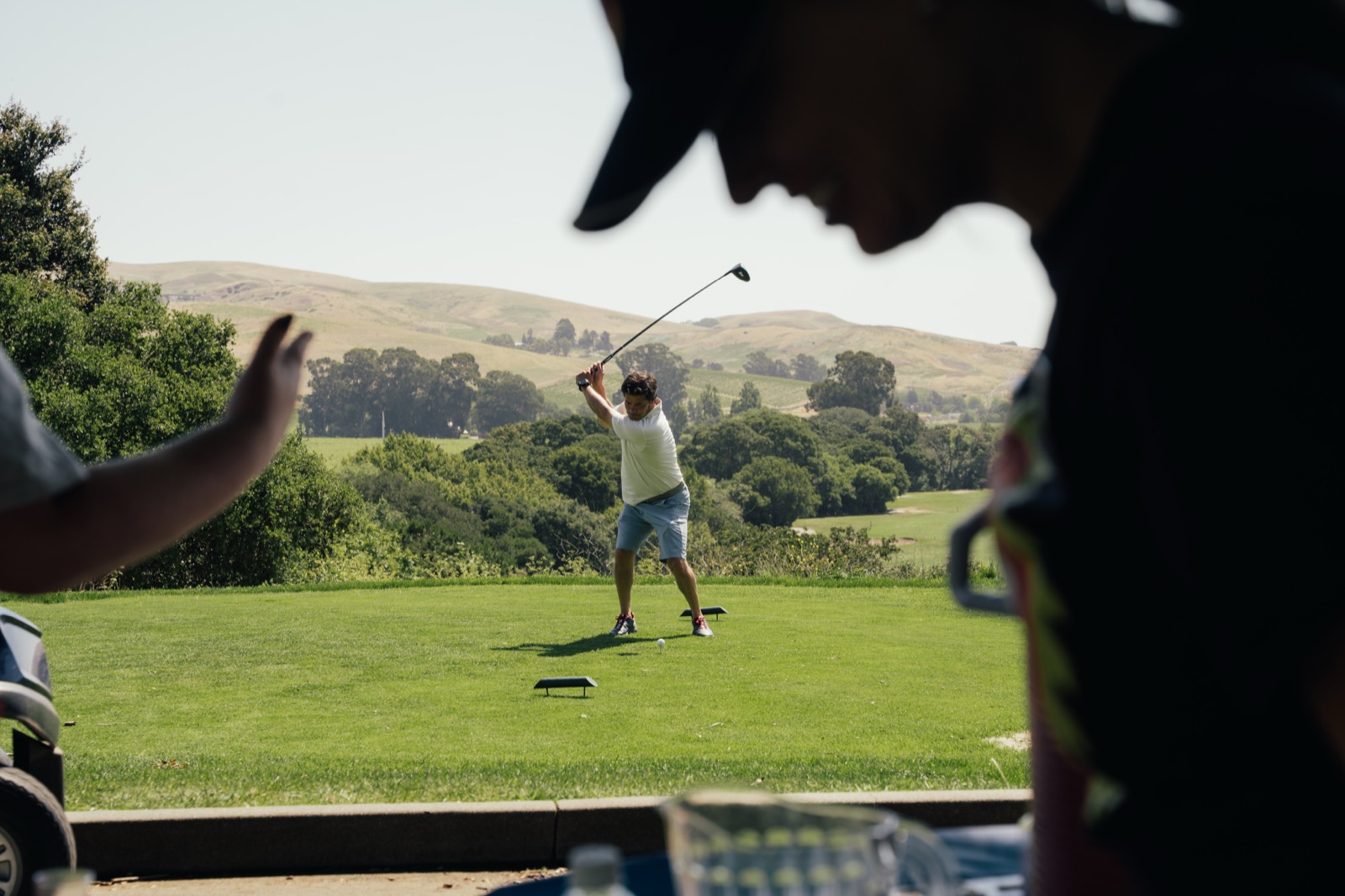 Golfer in follow-through swing with observers in casual setting