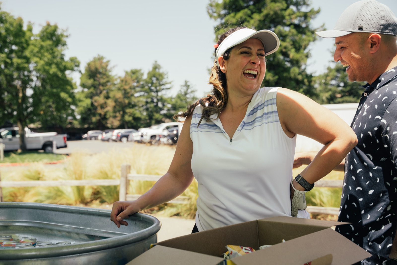 Man and woman both laughing while operating a cornhole game under a green tent.