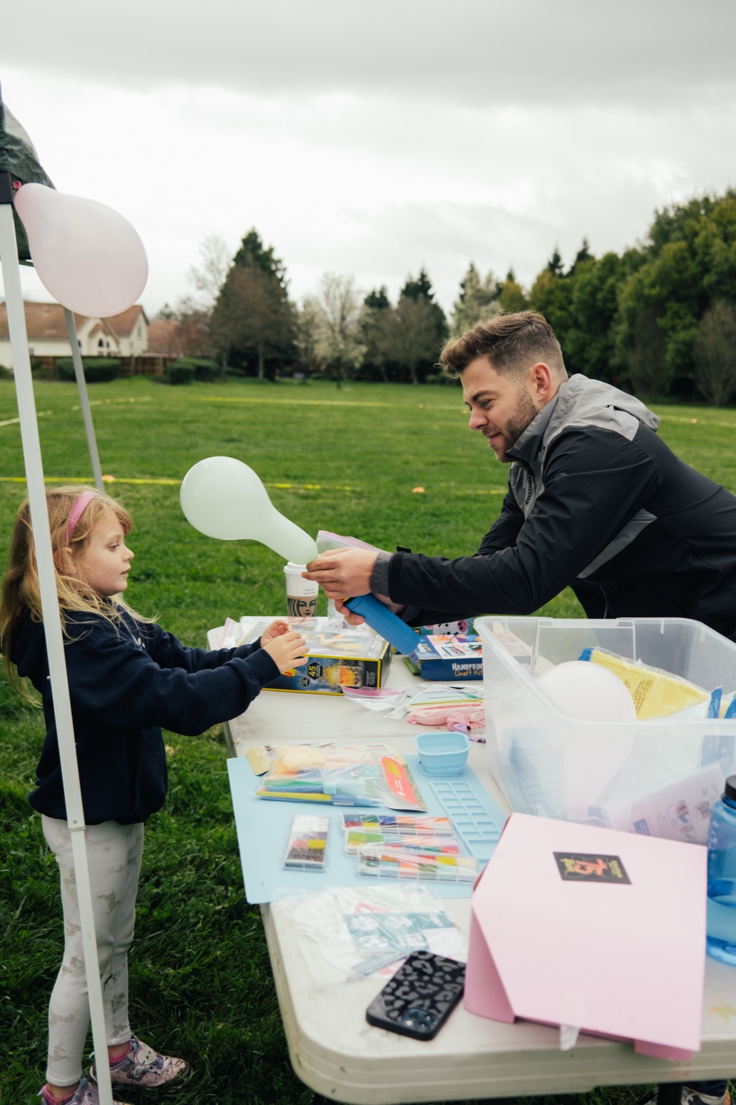 A volunteer engaging with a young child at a craft station with white balloons and activity materials.