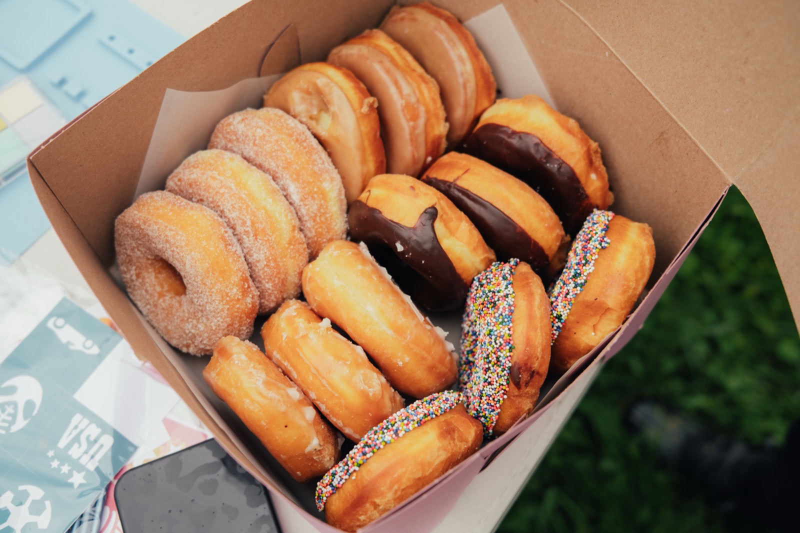 Colorful assorted donuts and pastries arranged in a cardboard box at a community event.