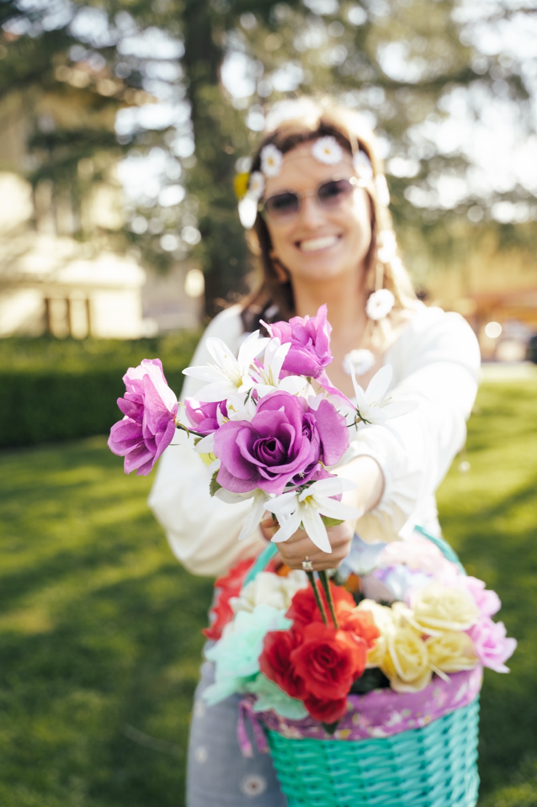 Woman with daisies in hair beaming while holding multicolored flower arrangement