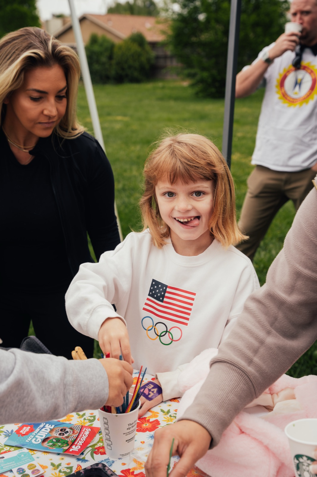 Happy child wearing flag shirt surrounded by smiling adult volunteers at craft activity