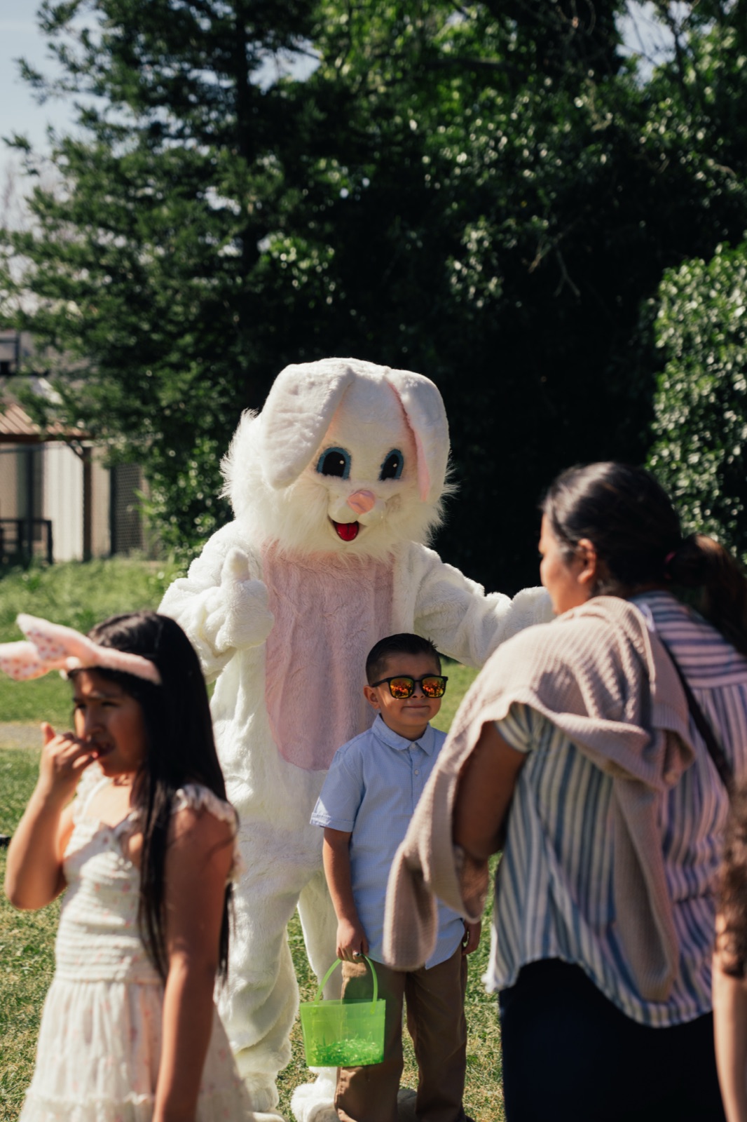 Easter Bunny mascot in playful interaction with group of children in sunny park setting.
